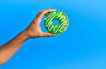 Wall Mural - Hand of hispanic man holding donut over isolated blue background.