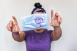 © AliciaFdez - Mujer vestida de morado sosteniendo una mascarilla desechable para el virus Sars-CoV-2 con el símbolo de la mujer. Día internacional de la Mujer en pandemia. Concepto de feminismo e igualdad de género