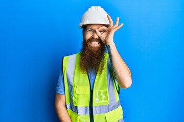 Poster - Redhead man with long beard wearing safety helmet and reflective jacket doing ok gesture with hand smiling, eye looking through fingers with happy face.