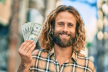 Wall Mural - Young caucasian man smiling happy holding usa dollars at the city.