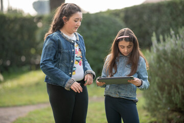 Canvas Print - Two young girls using tablets standing in the city park