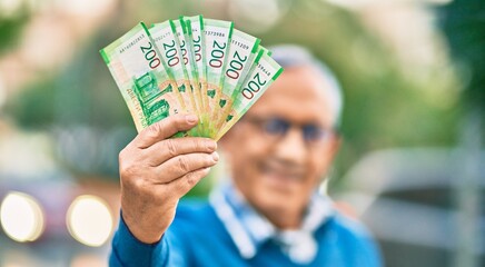 Wall Mural - senior grey-haired man smiling happy holding russian ruble banknotes at the city.