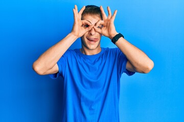 Young caucasian man wearing casual blue t shirt doing ok gesture like binoculars sticking tongue out, eyes looking through fingers. crazy expression.