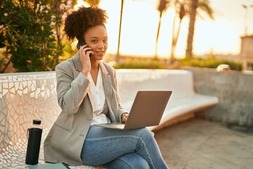 Canvas Print - Young african american businesswoman working using laptop sitting and talking on the smartphone.