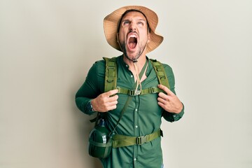 Poster - Handsome man with beard wearing explorer hat and backpack angry and mad screaming frustrated and furious, shouting with anger. rage and aggressive concept.