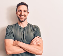 Young handsome man wearing casual t-shirt standing over isolated white background happy face smiling with crossed arms looking at the camera. Positive person.