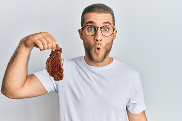 Canvas Print - Young caucasian man holding beef steak scared and amazed with open mouth for surprise, disbelief face