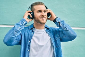 Sticker - Young caucasian man smiling happy using headphones at the city.