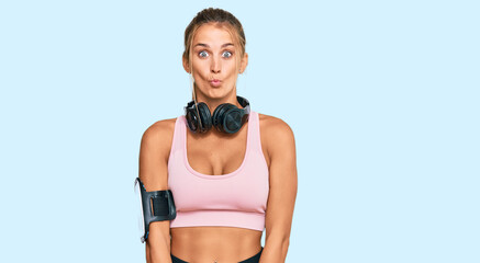 Wall Mural - Young blonde woman wearing gym clothes and using headphones making fish face with lips, crazy and comical gesture. funny expression.