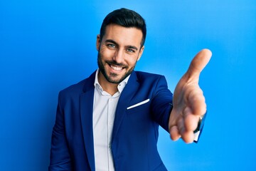 Canvas Print - Young hispanic businessman wearing business jacket smiling friendly offering handshake as greeting and welcoming. successful business.