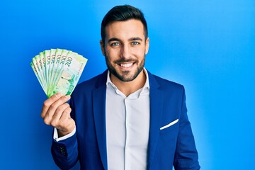 Young hispanic businessman wearing business suit holding russian ruble banknotes looking positive and happy standing and smiling with a confident smile showing teeth