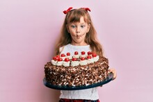 Little Caucasian Girl Kid Celebrating Birthday Holding Big Chocolate Cake Making Fish Face With Mouth And Squinting Eyes, Crazy And Comical.