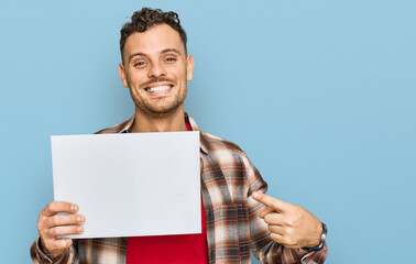 Canvas Print - Young hispanic man holding blank empty banner smiling happy pointing with hand and finger