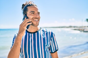 Young hispanic man smiling happy talking on the smartphone at the beach.