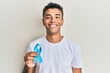 © Krakenimages.com - Young handsome african american man holding blue ribbon looking positive and happy standing and smiling with a confident smile showing teeth