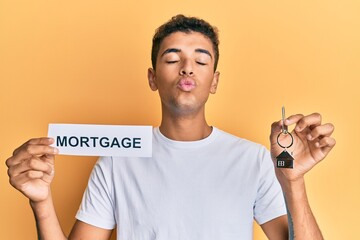 Poster - Young handsome african american man holding paper with mortgage word and house keys looking at the camera blowing a kiss being lovely and sexy. love expression.