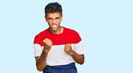 Wall Mural - Young handsome african american man wearing casual clothes angry and mad raising fist frustrated and furious while shouting with anger. rage and aggressive concept.