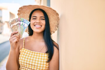 Young asian girl smiling happy at the city holding canadian dollars banknotes