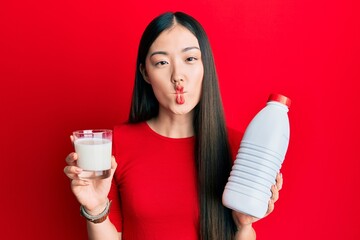 Poster - Young chinese woman drinking a glass of fresh milk making fish face with mouth and squinting eyes, crazy and comical.