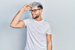 Young hispanic man with modern dyed hair wearing white t shirt and glasses smiling confident touching hair with hand up gesture, posing attractive and fashionable
