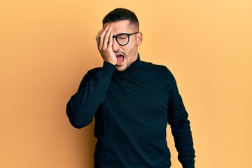 Poster - Handsome man with tattoos wearing turtleneck sweater and glasses yawning tired covering half face, eye and mouth with hand. face hurts in pain.