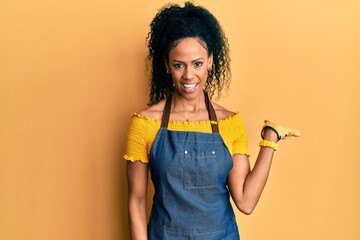 Poster - Middle age african american woman wearing professional apron smiling cheerful presenting and pointing with palm of hand looking at the camera.