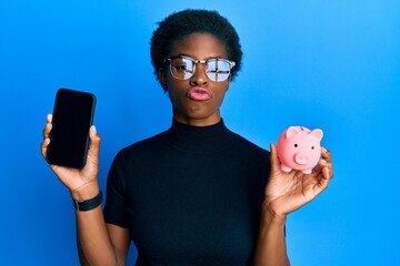 Poster - Young african american girl holding piggy bank and smartphone looking at the camera blowing a kiss being lovely and sexy. love expression.