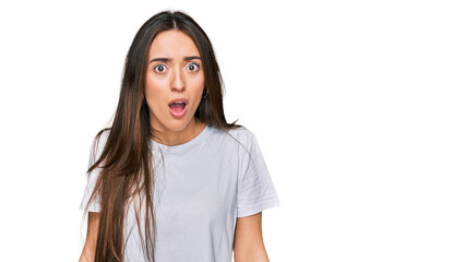 Wall Mural - Young hispanic girl wearing casual white t shirt afraid and shocked with surprise and amazed expression, fear and excited face.