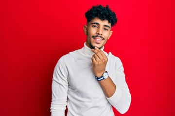 Wall Mural - Young arab handsome man wearing turtleneck sweater smiling looking confident at the camera with crossed arms and hand on chin. thinking positive.