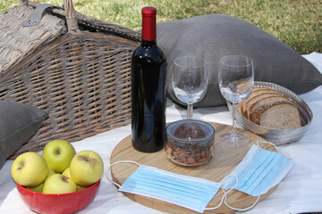 stylish picnic in pandemic. vintage basket with wine, food fruit seeds and protective masks clinical use