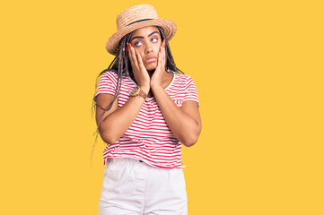 Wall Mural - Young african american woman with braids wearing summer hat tired hands covering face, depression and sadness, upset and irritated for problem