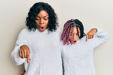 Canvas Print - Beautiful african american mother and daughter wearing casual winter sweater pointing down with fingers showing advertisement, surprised face and open mouth