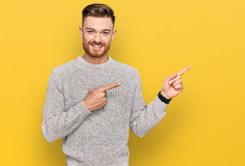 Young redhead man wearing casual winter sweater smiling and looking at the camera pointing with two hands and fingers to the side.