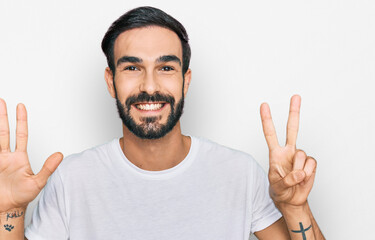 Young hispanic man wearing casual white t shirt showing and pointing up with fingers number seven while smiling confident and happy.