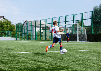 Wall Mural - Young sport boys in white sportswear running and kicking a  ball on pitch. Soccer youth team plays football in summer. Activities for kids, training	