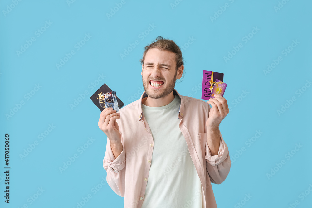 Happy young man with gift cards on color background