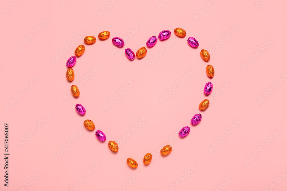 Heart made of sweet chocolate eggs on color background