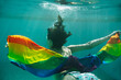 Horizontal view of unrecognizable woman swimming underwater holding a colorful lgbt flag. Lesbian, gay, bisexual and transgender iconic colors. Gay pride and summer holidays concept.