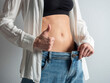 © Sergey - A slender girl with a bare stomach shows how she lost weight. Jeans is large in size. Thumbs up, the concept of diet, weight loss, beauty