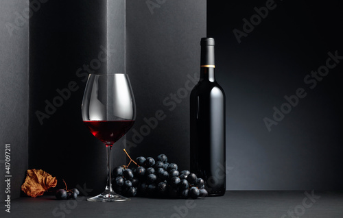 Red wine and blue grapes with dried up vine leaves on a black background. © Igor Normann