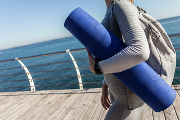 Wall Mural - Sport woman holding mat on the beach on a bright sunny day