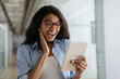 © ARUTA Images - Happy excited African American woman using digital tablet reading good news, watching videos. Young overjoyed female shopping online with big sales and cash back