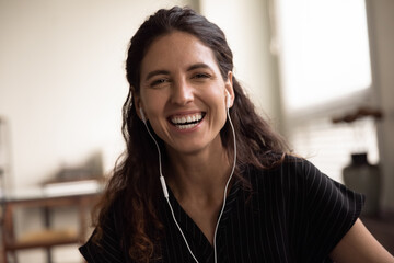 Wall Mural - Head shot portrait overjoyed woman wearing earphones laughing at camera, excited happy young female making video call, enjoying pleasant conversation, blogger recording vlog, having fun with webcam