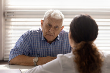 Close up anxious serious old man listening to female doctor at meeting in hospital, therapist physician consulting mature patient about disease, treatment, elderly generation healthcare concept