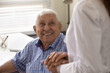 © fizkes - Close up smiling mature man and female caregiver wearing white uniform holding hands, doctor nurse comforting and supporting senior patient at meeting in hospital, expressing empathy and care