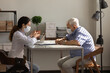 © fizkes - Side view female doctor wearing medical face mask consulting elderly man about treatment at meeting in hospital, therapist and senior patient discussing checkup results, health insurance contract