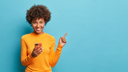 horizontal shot of happy dark skinned afro american woman enjoys mobile communication and modern tec