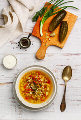 Wall Mural - Thick hearty Pickle soup with vegetables (pickles, cucumbers, carrots, onions, potatoes, tomatoes, dill) and pearl barley in a white plate on a wooden table. Rassolnik. Dish of Russian cuisine