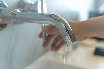 Save the water concept.Hand closing valve on sink in bathroom. Water dripping to stop running as hand turn off the faucet. Detect a Leak week.