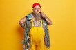© wayhome.studio  - Photo of thoughtful plump seaman poses with fishing net smokes pipe raises eyebrows has pensive expression dressed in overalls tattooed body isolated over yellow background. Sea life concept